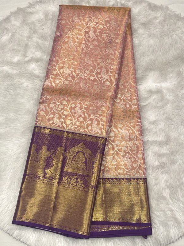 Elegant Pastel Peach Kanjivaram Saree with all-over silver/gold floral brocade on the body, contrasted dramatically by a broad, Deep Purple border featuring traditional Gold Zari Temple and figurative motifs.
