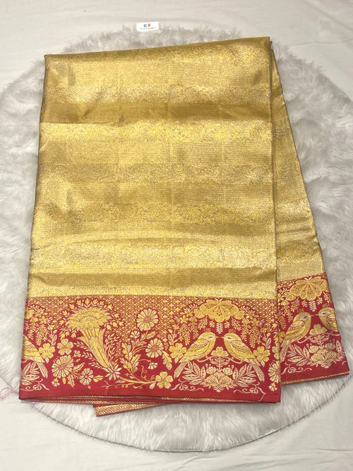 Opulent Pure Gold Tissue Kanjivaram Saree with a self-woven texture on the body, contrasted beautifully by an extra-wide, heavy Red Brocade border featuring large, traditional Bird (Peacock/Hamsa) and floral motifs woven in Gold Zari.