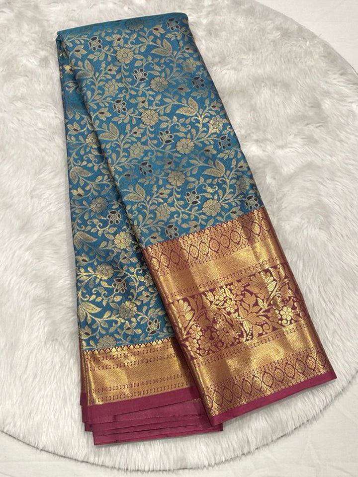 Sky Blue Kanjivaram Pattu Saree with all-over Gold Zari floral brocade, finished with a broad Contrast Magenta Zari border.