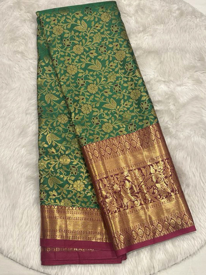 Emerald Green Pattu Saree with all-over Gold Zari floral brocade, framed by a broad Contrast Magenta border featuring traditional Zari motifs.