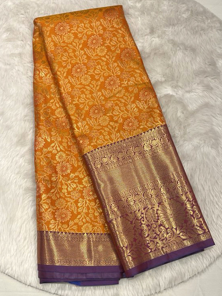 Vibrant Orange Pattu Saree with all-over Gold Zari floral brocade, set against a magnificent Contrast Violet Zari Brocade border.